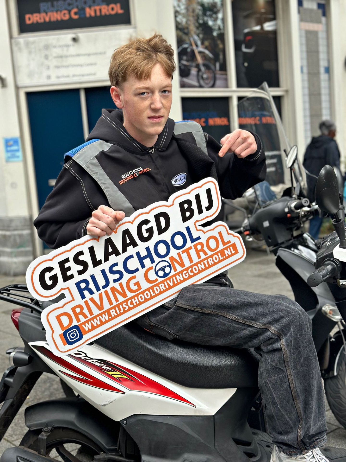 Geslaagde scooterleerling Bram op scooter met Geslaagd-bord Rijschool Driving Control Rotterdam